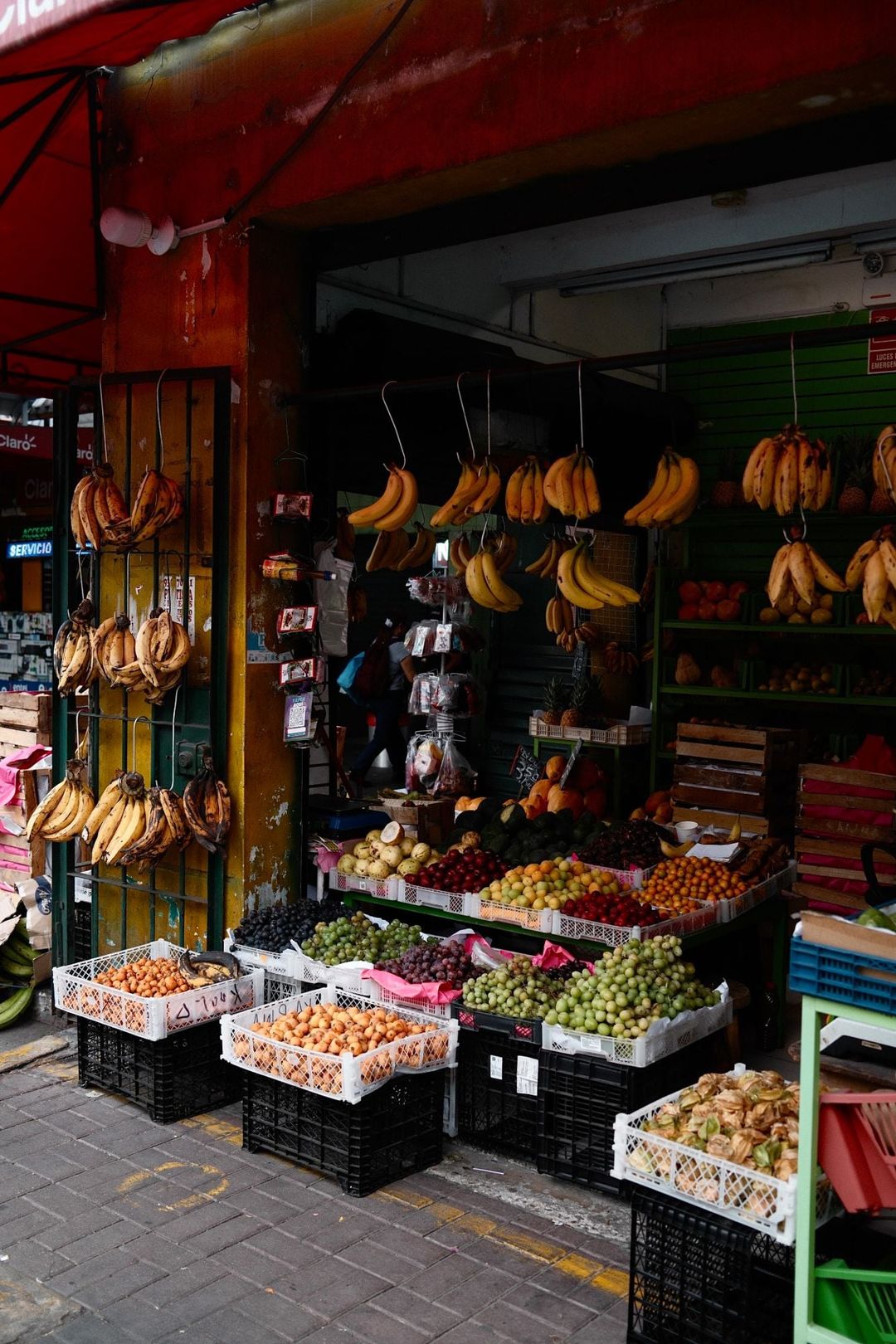A fruit stall in a Lima market street with bunches of bananas hanging from hooks and crates of grapes, plums and loquats on the pavement